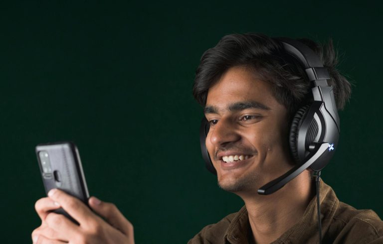Smiling young man using a smartphone with headphones, enjoying music indoors.